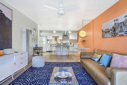 A stylish and vibrant open-concept living space featuring a modern sofa, colorful accents, and a well-equipped kitchen.