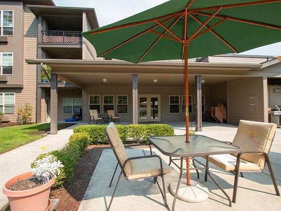 A cozy outdoor patio area with a table and chairs under a large umbrella, set against the backdrop of a modern building.
