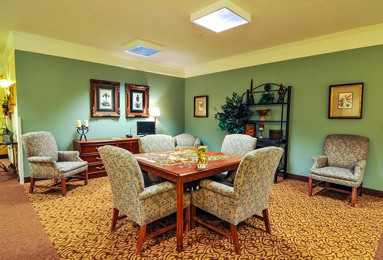 A cozy living room with a seating area centered around a wooden table and upholstered chairs, complemented by decorative elements and soft lighting.