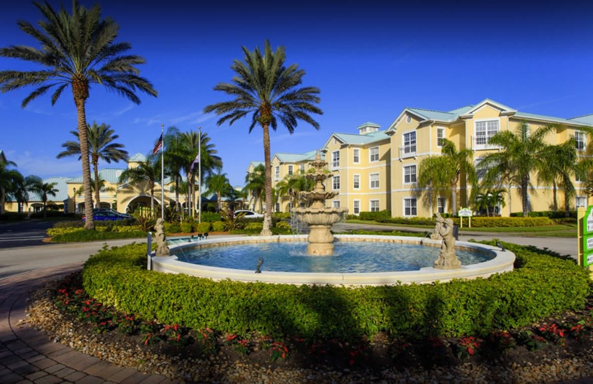 A beautiful apartment complex with a central fountain and lush landscaping under a clear blue sky.