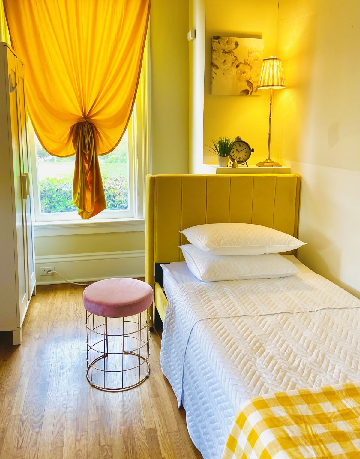 A cozy bedroom with vibrant yellow decor, featuring a single bed and a small stool by the window.