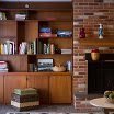 A cozy living room with wooden shelves filled with books and decorative items next to a brick fireplace.
