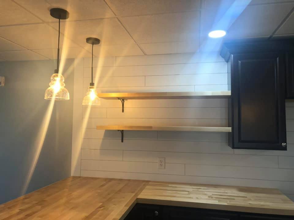 A modern kitchen with wooden shelves, a wooden countertop, and pendant lighting.