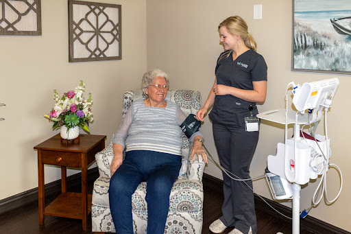 A nurse checks the blood pressure of an elderly patient in a comfortable indoor setting.