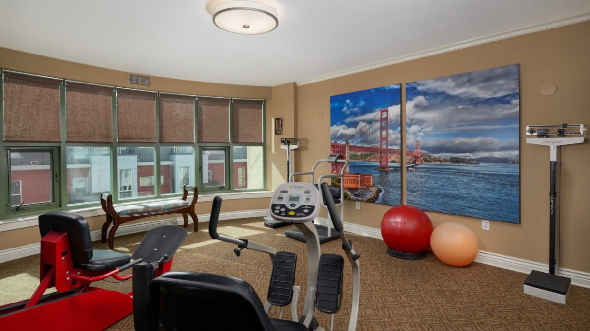 A fitness room featuring various exercise equipment, including a stationary bike and yoga balls, with a mural of San Francisco on the wall.