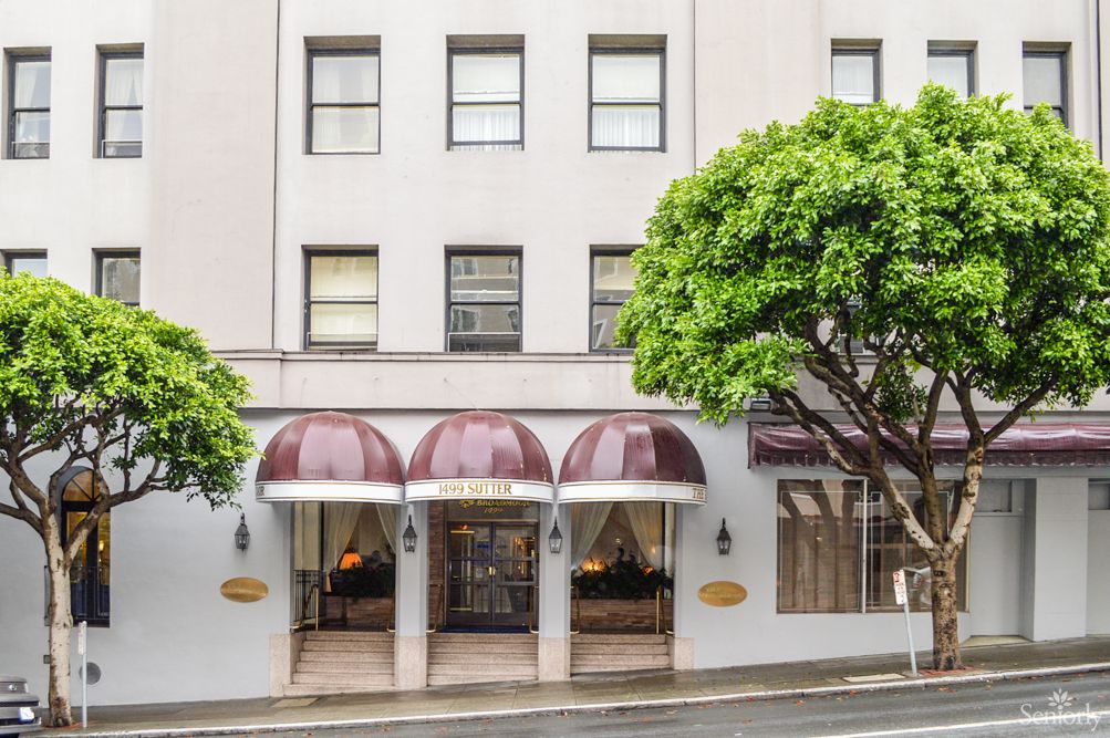 Facade of a hotel with maroon awnings and trees on the sidewalk.