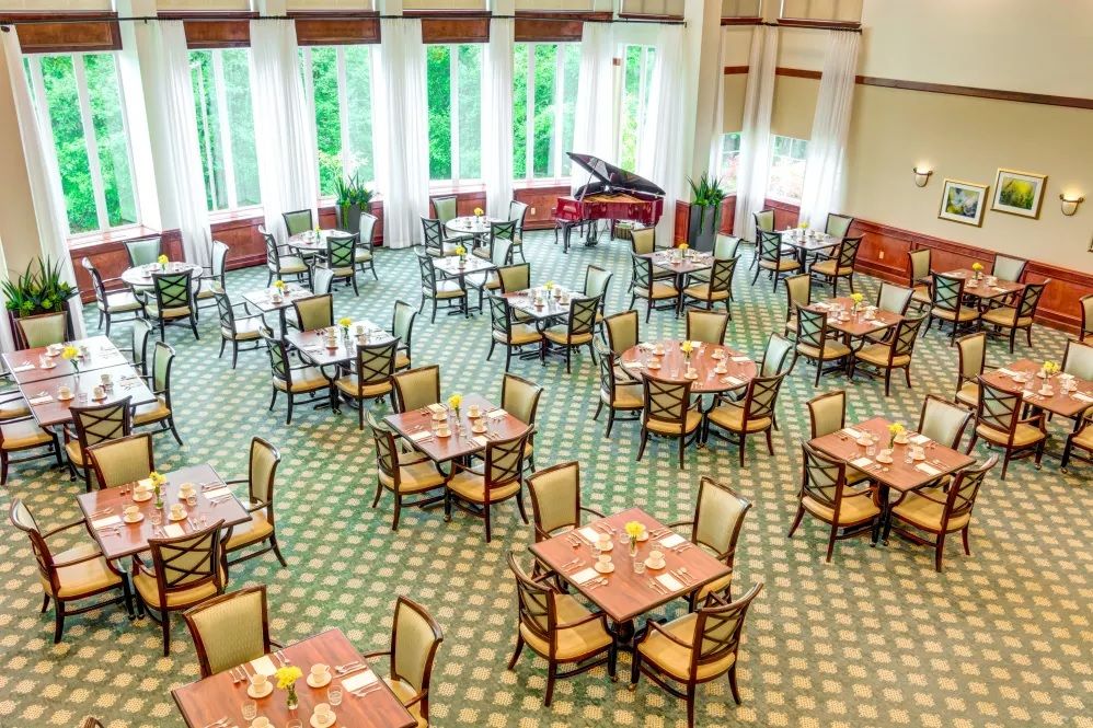 An elegant dining room with neatly arranged tables and a grand piano by the window.