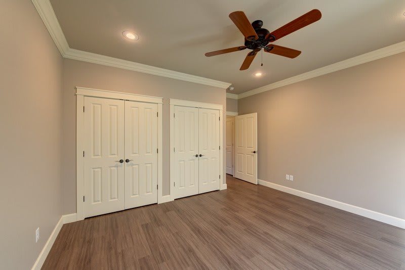 A spacious empty room with wood flooring, featuring dual closets, a ceiling fan, and recessed lighting.