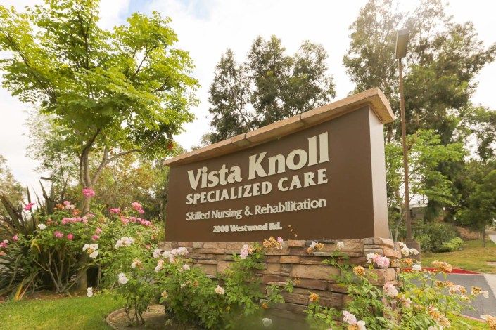 A sign for Vista Knoll Specialized Care, a skilled nursing and rehabilitation facility, surrounded by greenery.