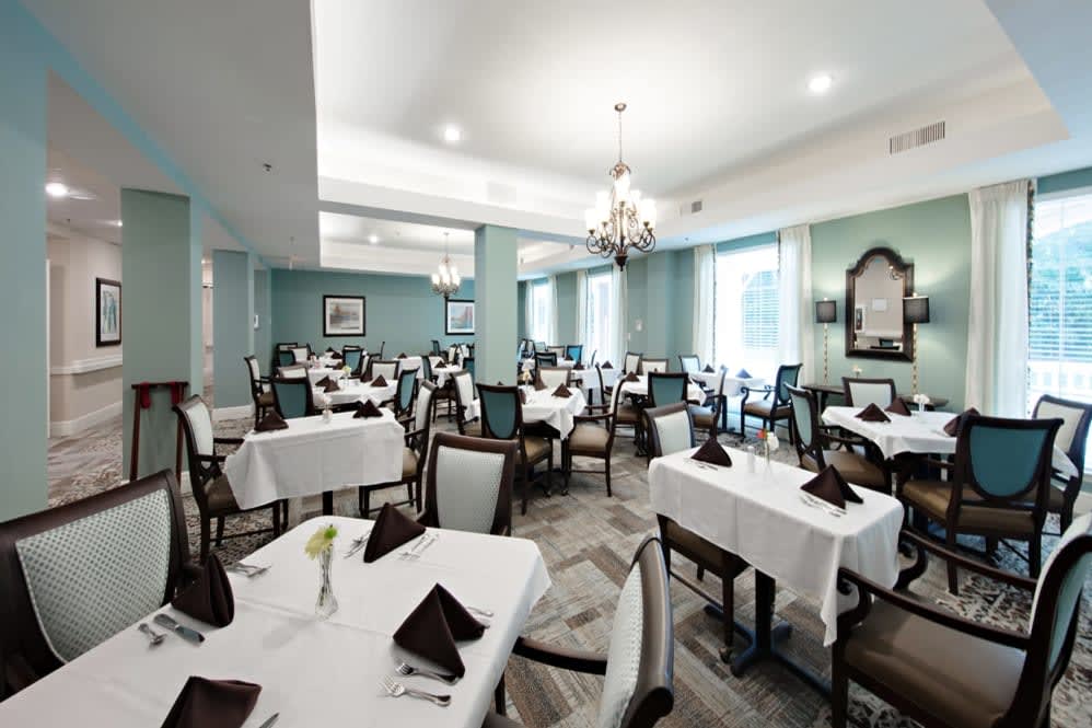 An elegant dining room with neatly arranged tables and chairs, featuring white tablecloths and a chandelier.