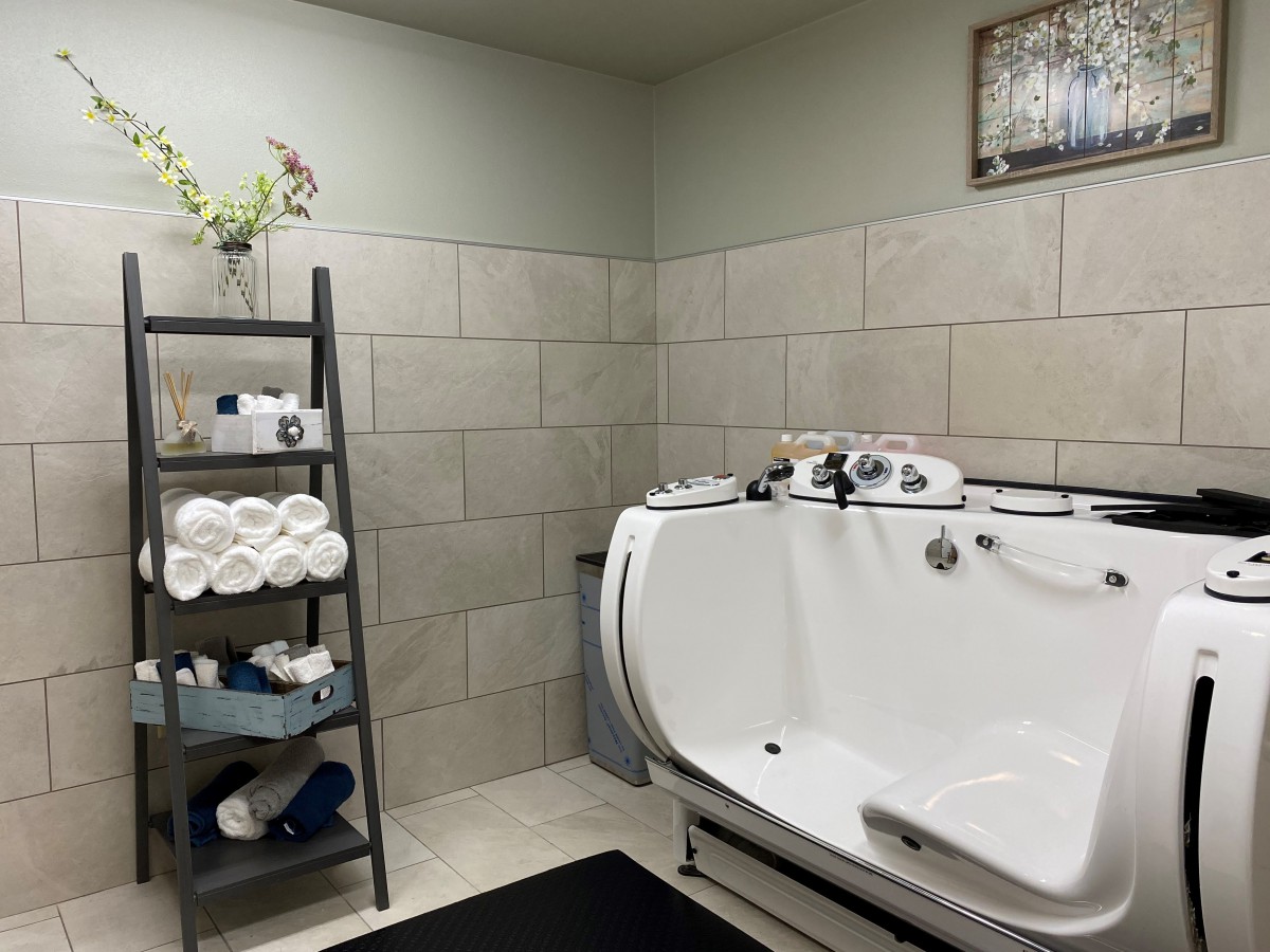 A modern bathroom featuring a sleek bathtub, neatly arranged towels on a shelf, and stylish tile walls.