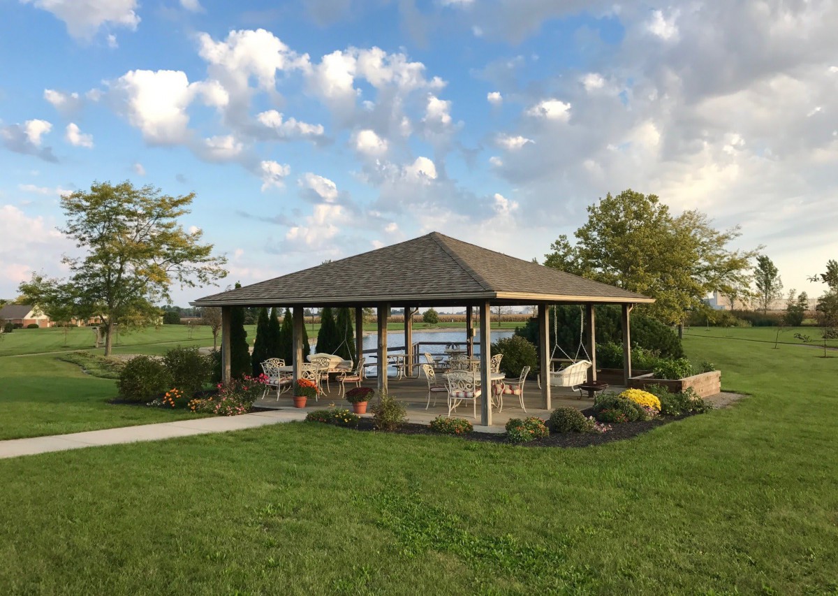 A serene outdoor pavilion surrounded by lush greenery and an expansive sky.