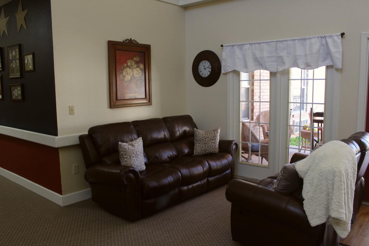 A cozy living room with brown leather sofas, wall art, and a large window.