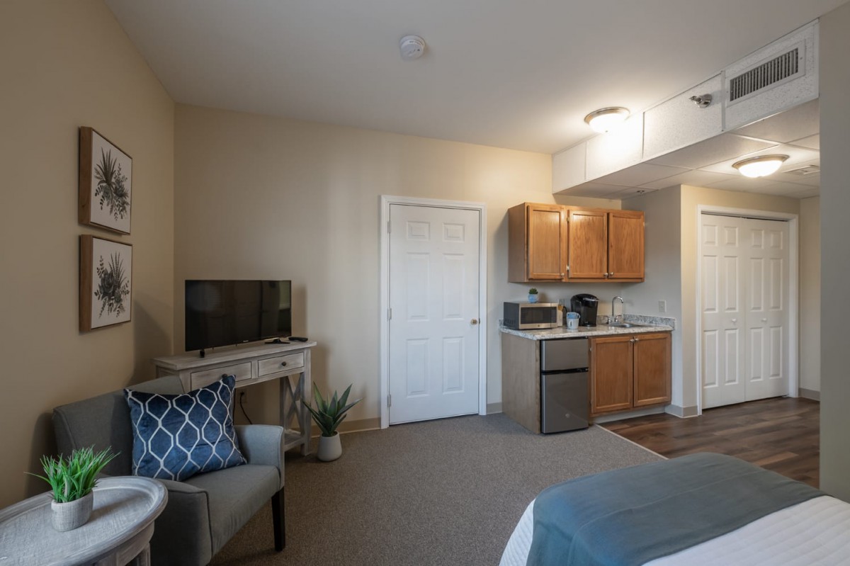 A cozy studio apartment featuring a kitchenette and a small seating area with a television.