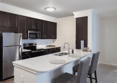 A modern kitchen with dark cabinets and stainless steel appliances, featuring a white countertop island with seating.