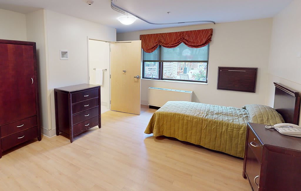 A simple bedroom with a single bed, dresser, and window with curtains.