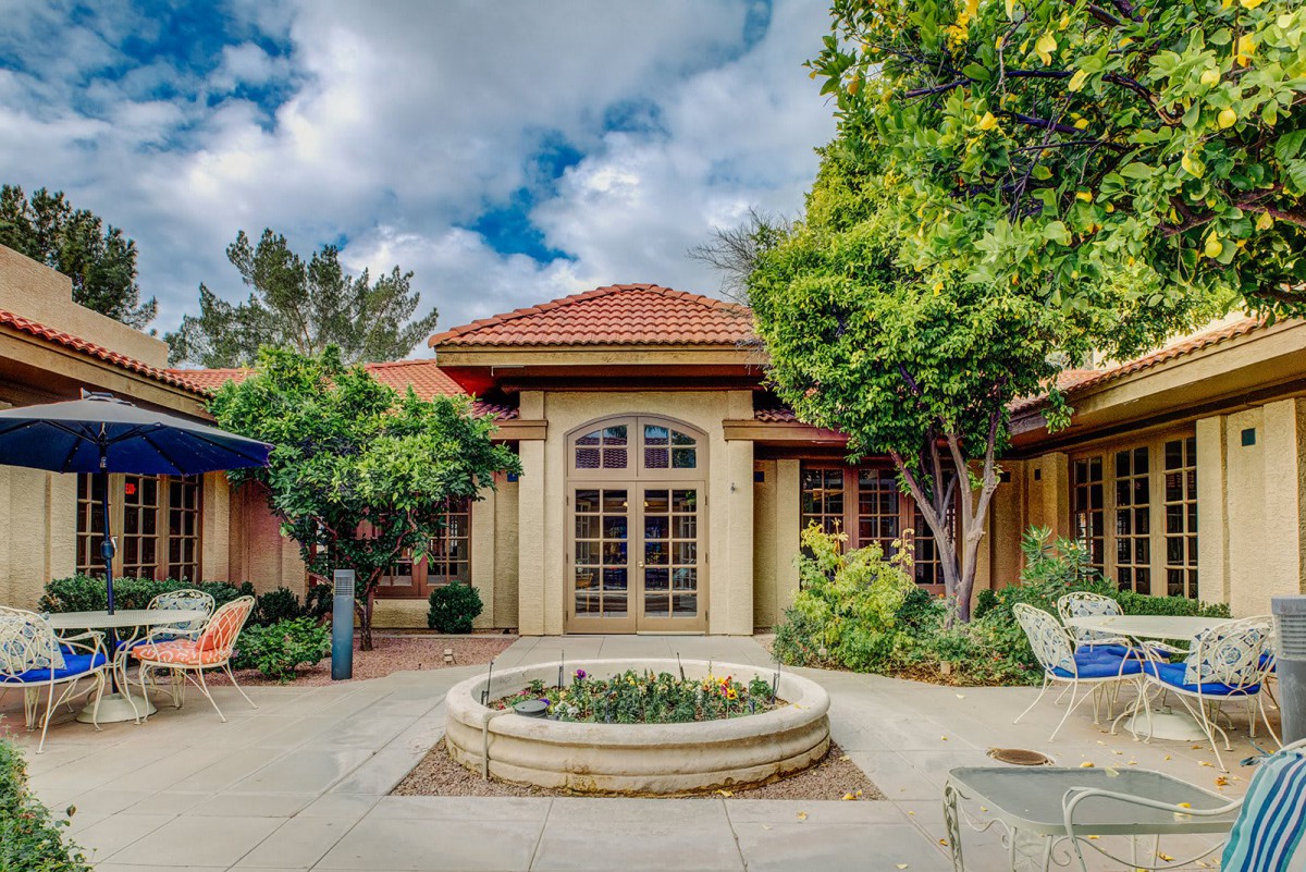 A picturesque view of a courtyard with a central garden and trees, surrounded by a house with red-tiled roofs under a partly cloudy sky.