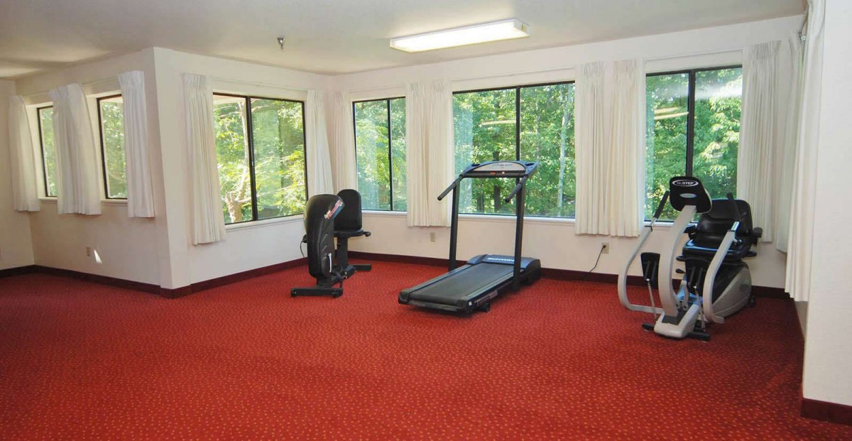 A well-lit exercise room with a treadmill and other fitness equipment situated near large windows.