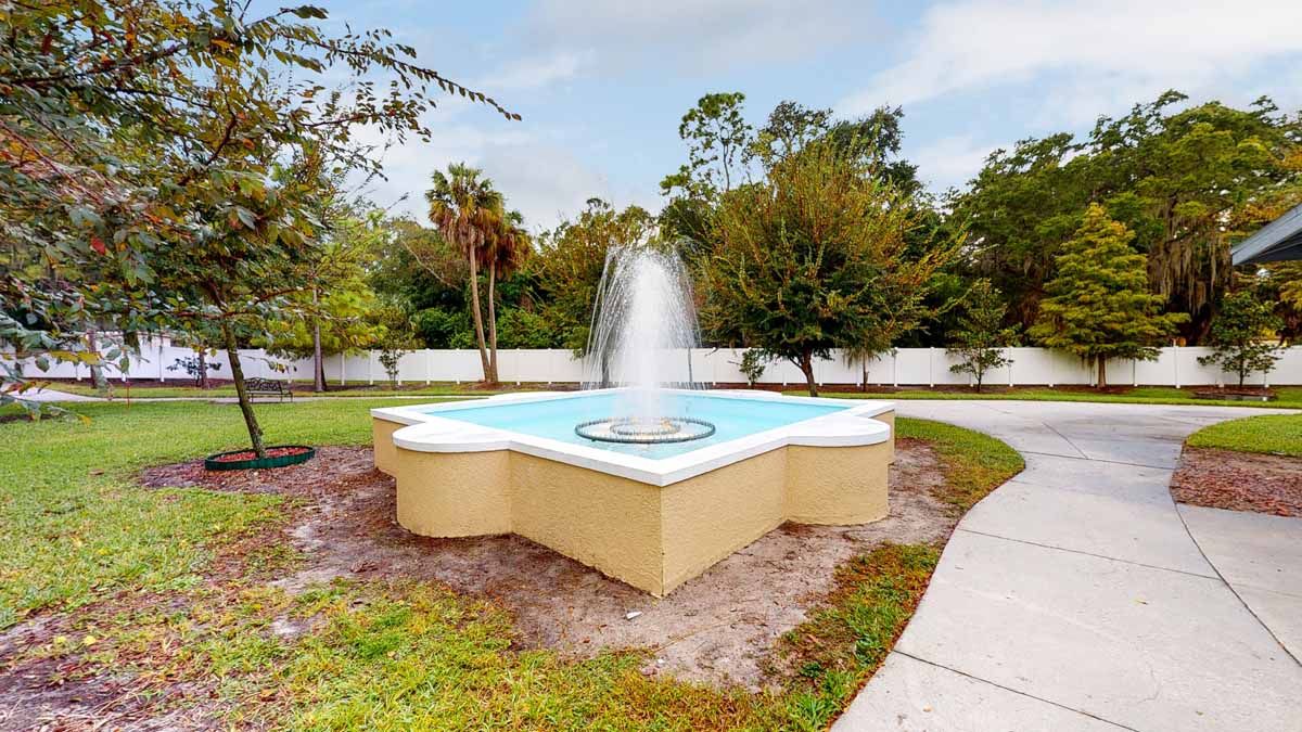 A decorative outdoor fountain surrounded by trees and a pathway in a garden setting.