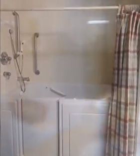 A bathroom shower area with a plaid curtain and safety grab bar.