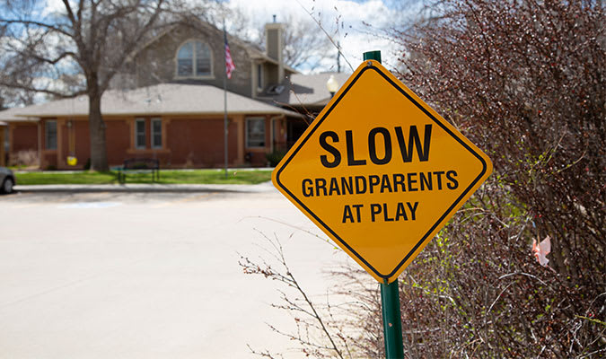 A humorous street sign warns 'Slow, Grandparents at Play' in a suburban neighborhood.