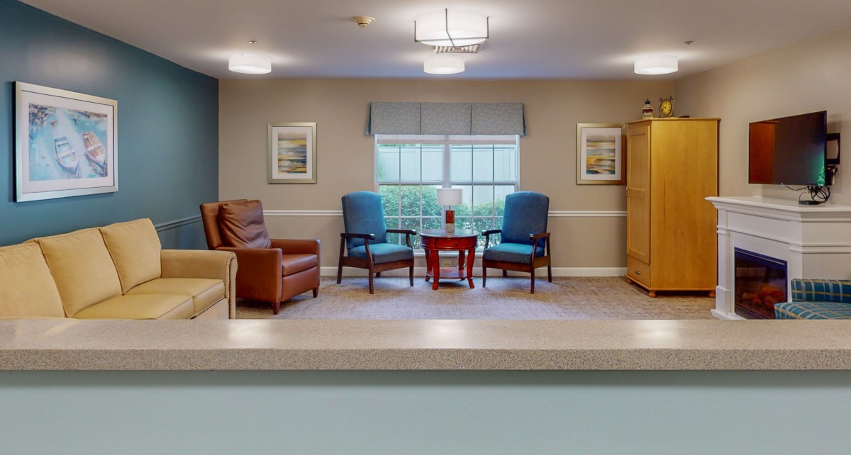 A cozy living space featuring a pair of blue chairs and a brown leather chair arranged around a small wooden table, set in front of a large window with framed artwork on the walls.