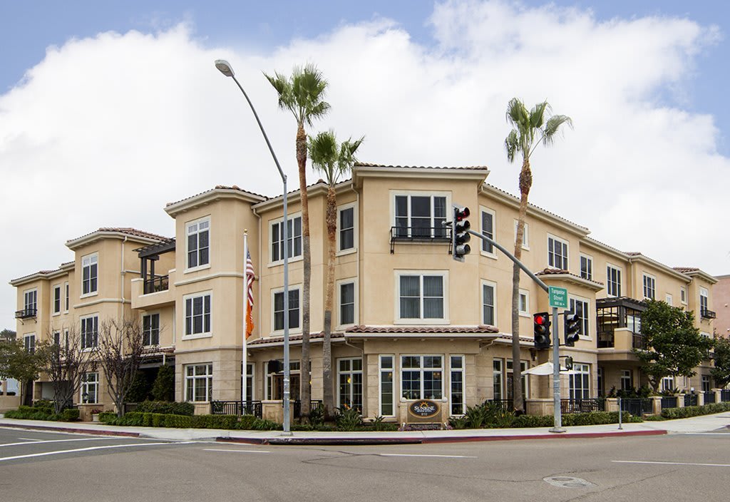A modern residential building at a street intersection, surrounded by palm trees.
