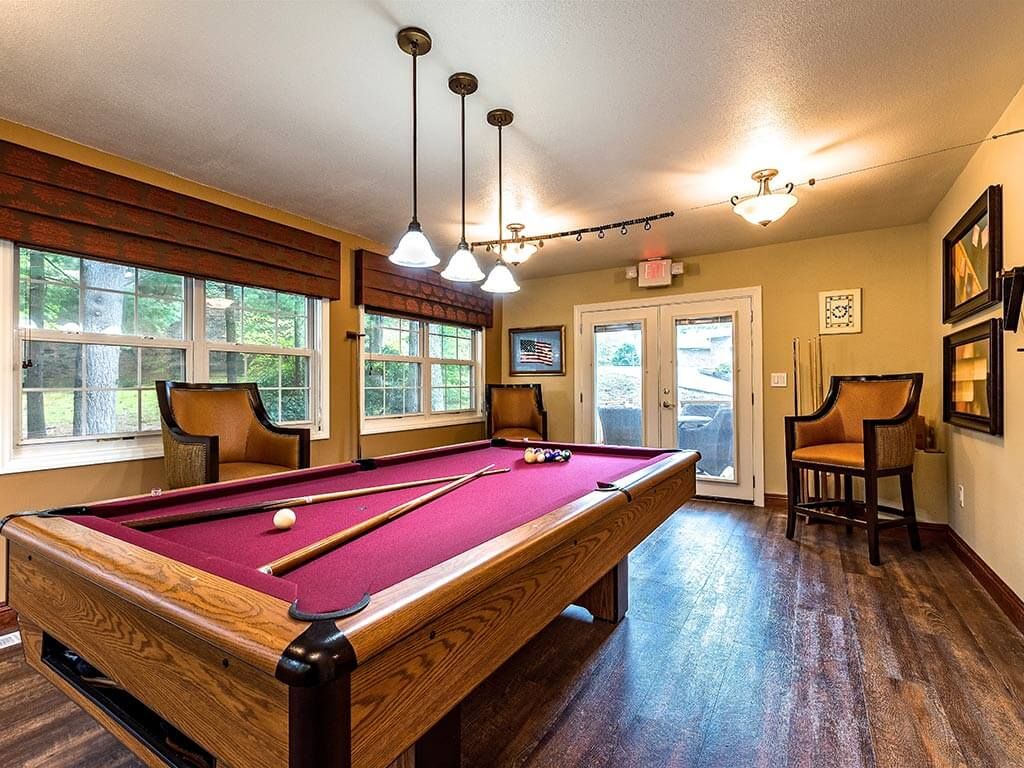 A cozy game room featuring a pool table with wooden chairs and warm lighting.