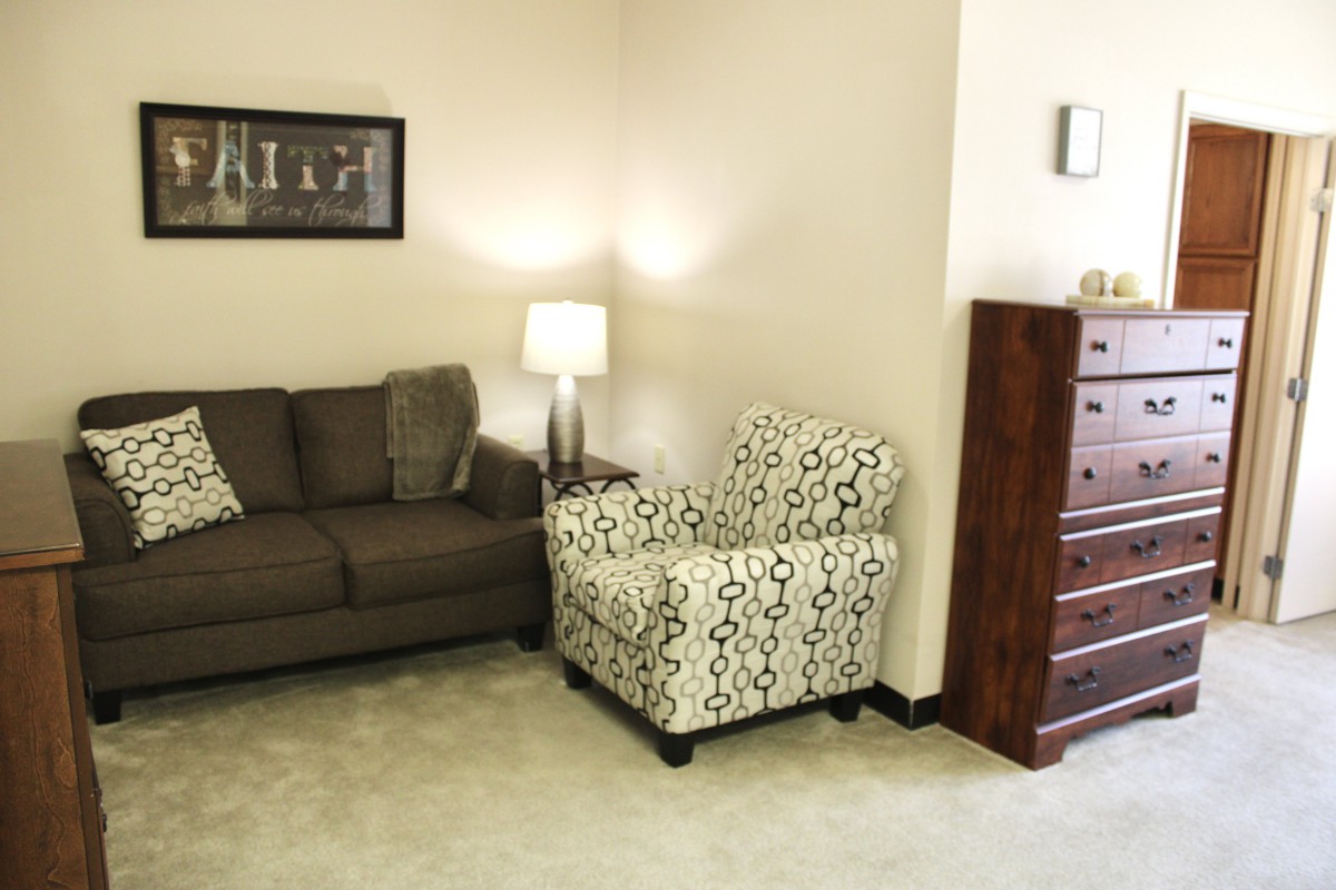 A cozy living room with a sofa, patterned armchair, and a wooden dresser.