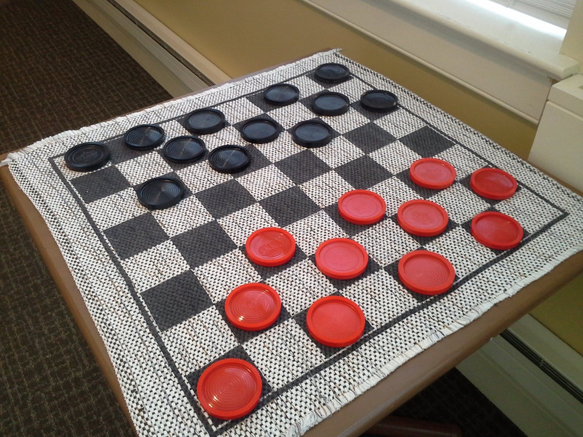 A checkers board set up with red and black pieces on a table.