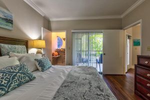 A cozy bedroom featuring a large bed with decorative pillows, soft lighting from a bedside lamp, and a sliding door leading to a balcony.