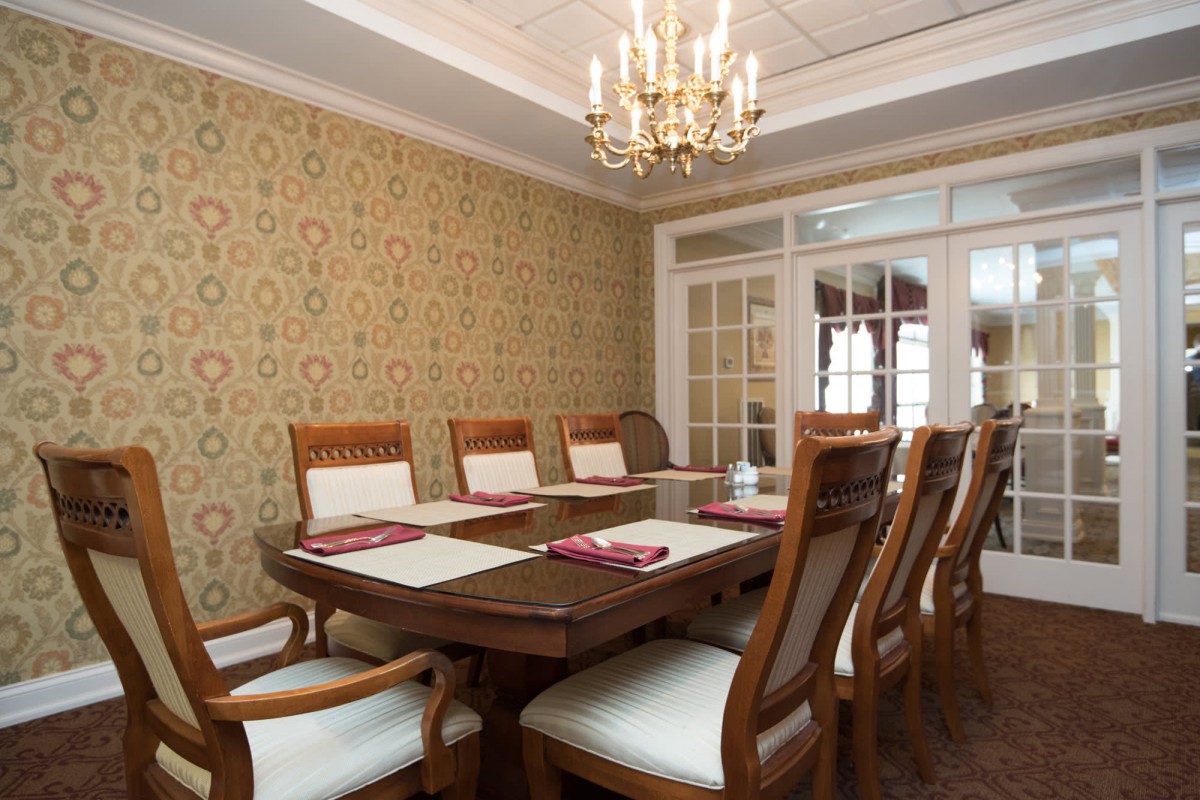 An elegant dining room featuring a wooden table with upholstered chairs, ornate wallpaper, and a chandelier.