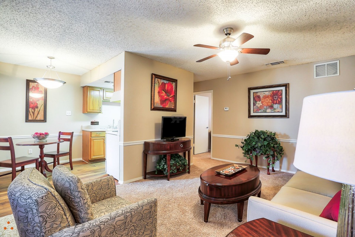 A cozy living room with comfortable seating, a coffee table, and a television, decorated with artwork and plants.