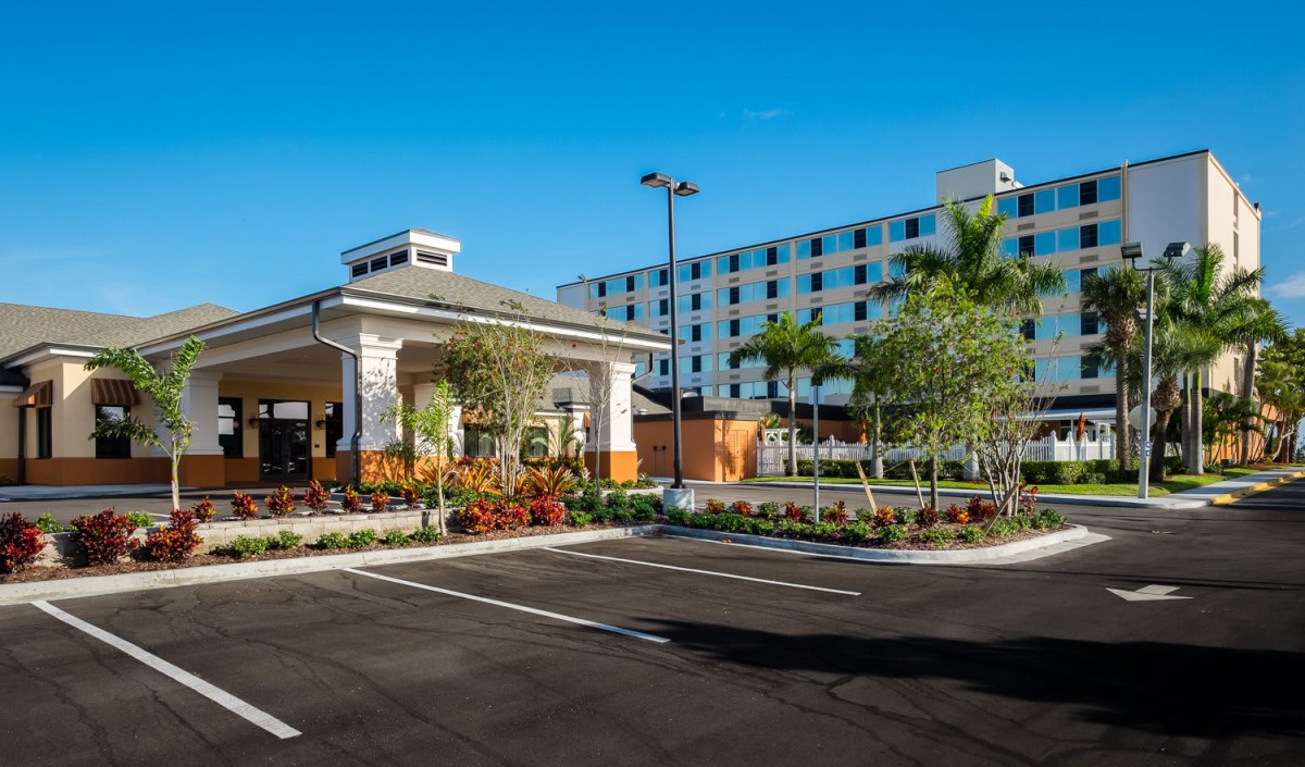 A modern hotel building with a well-maintained parking lot, surrounded by palm trees on a sunny day.