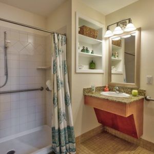 A cozy bathroom featuring a walk-in shower with a curtain, a sink with an overhead mirror, and neatly arranged shelves.