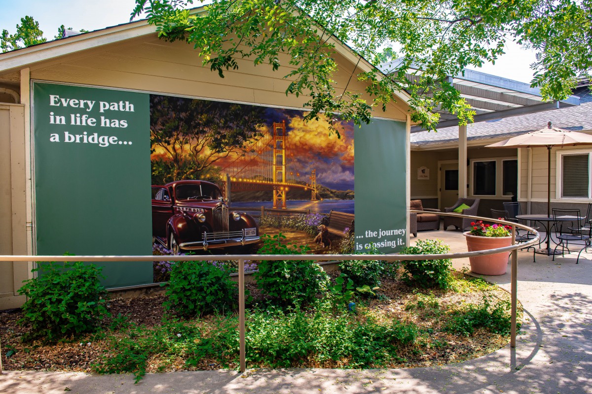 A building exterior featuring a mural depicting a scenic landscape, surrounded by greenery.