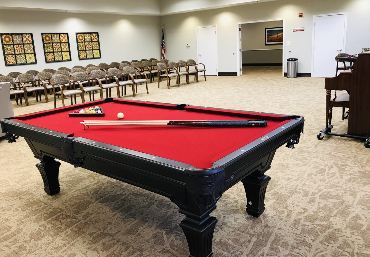 A spacious recreation room featuring a red-felt pool table and neatly arranged chairs.