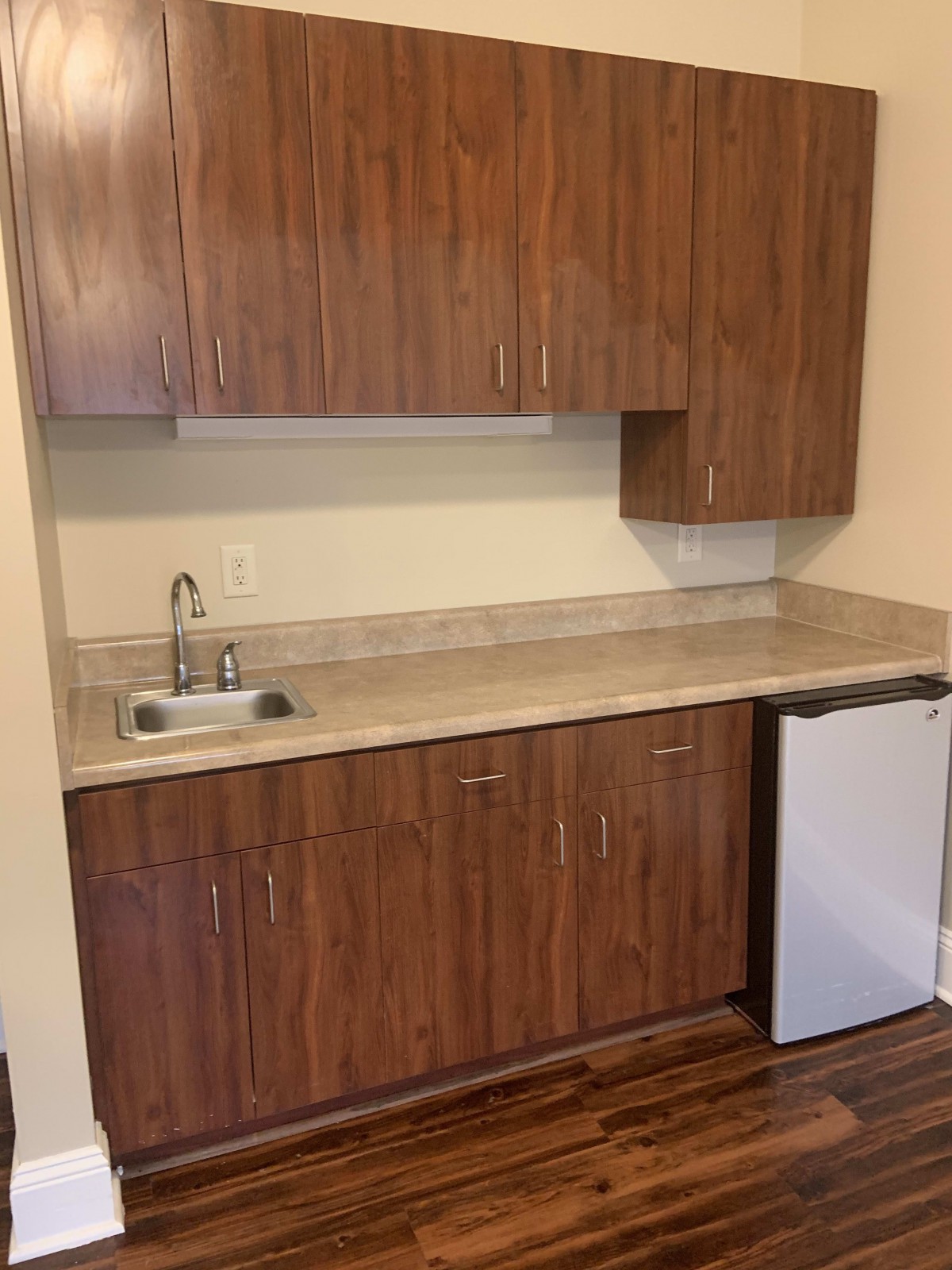 A small kitchenette featuring wooden cabinets, a countertop with a sink, and a mini fridge.