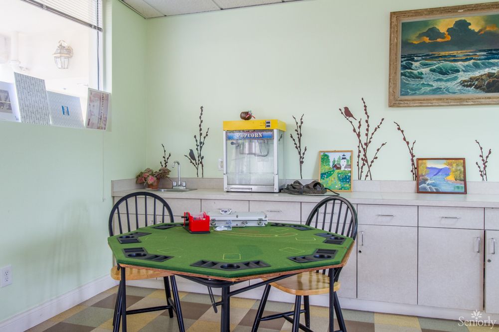 A cozy game room features a mahjong table surrounded by chairs, with a popcorn machine and decorative elements on the counter.