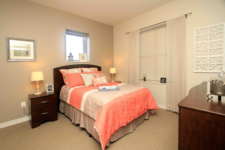 A cozy bedroom with a neatly made bed featuring coral and beige bedding, flanked by two bedside tables with lamps.