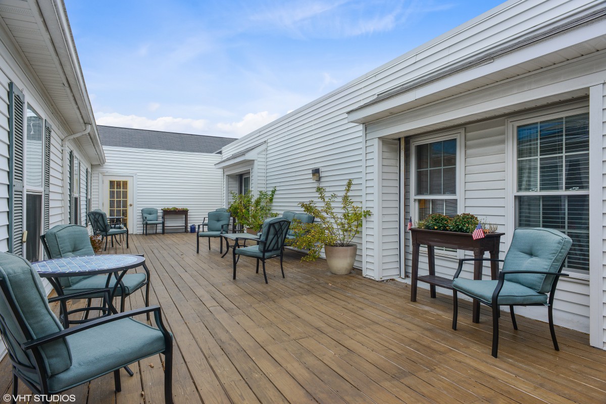 A spacious outdoor deck featuring seating arrangements and potted plants, set against a building exterior under a clear sky.