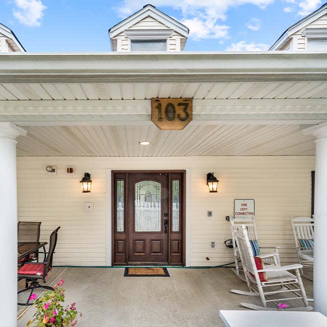 A welcoming porch with rocking chairs and a decorative front door, under a covered area displaying the number 103.