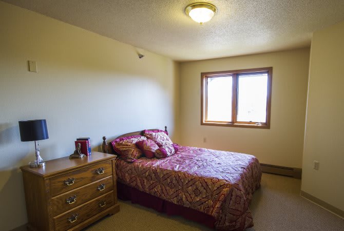 A simple bedroom with a bed, dresser, and window.