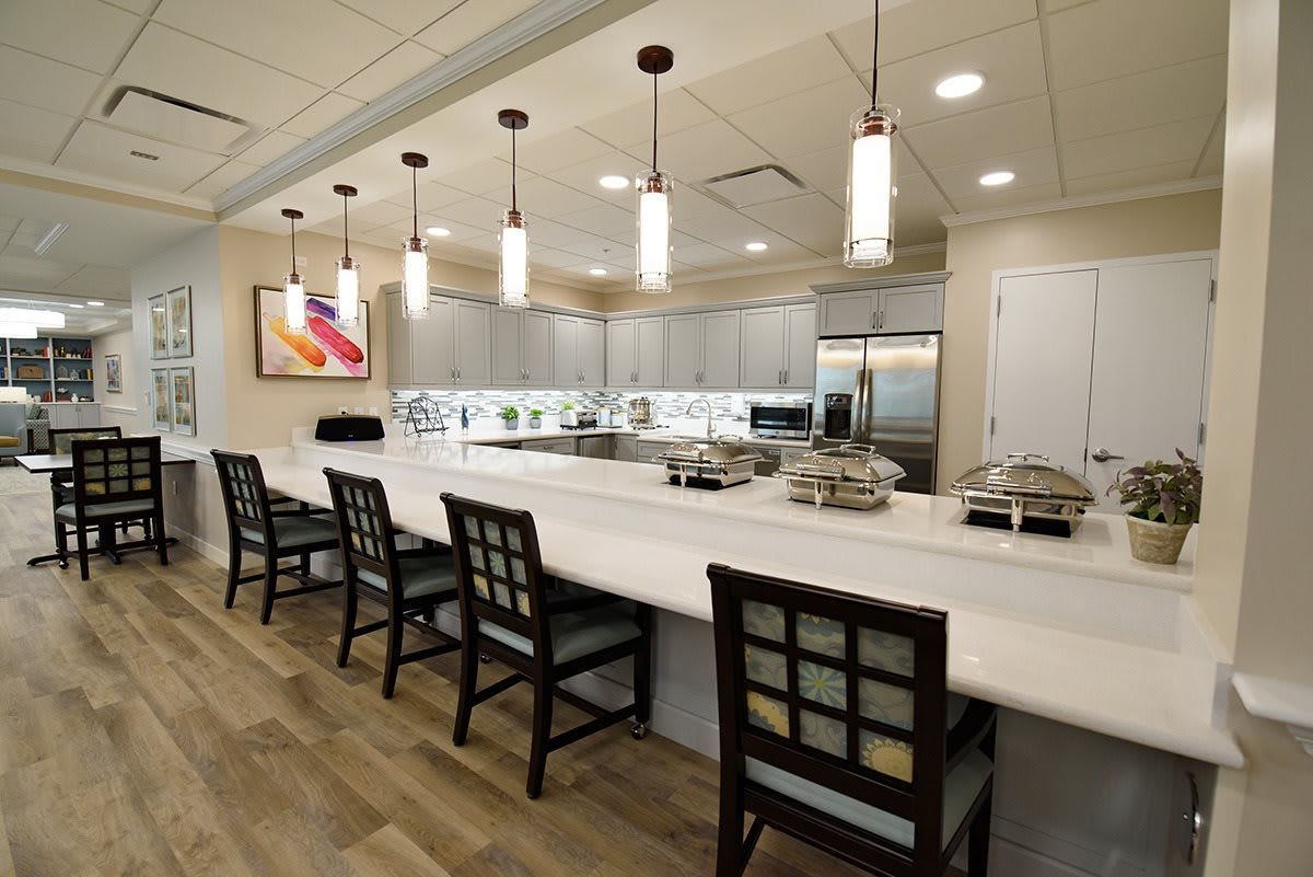 A modern kitchen with a long countertop, pendant lights, and seating area.