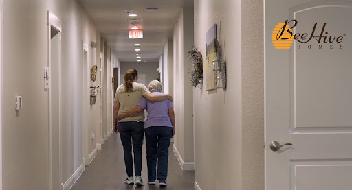 A caregiver gently assists an elderly woman down a quiet hallway, showcasing the importance of support and companionship.