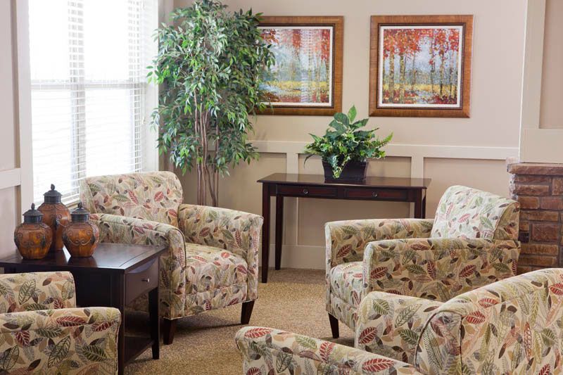 A cozy living room with floral-patterned chairs, indoor plants, and wall art.