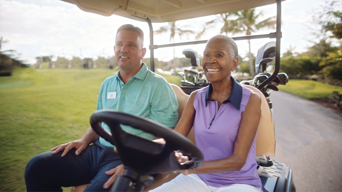 Two people enjoying a ride in a golf cart on a sunny day.