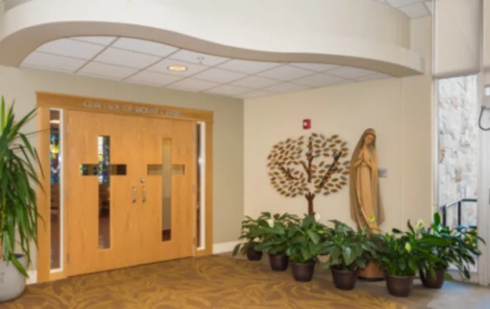 A serene interior view featuring a religious statue beside wooden doors and potted plants.