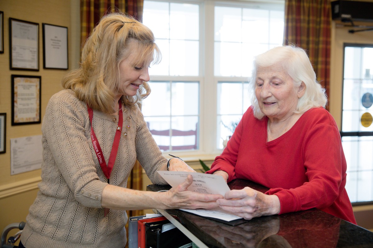 A caregiver assisting an elderly woman with paperwork in a cozy room.