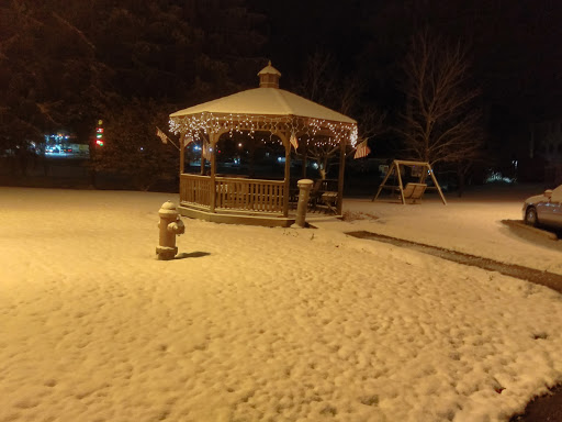 A peaceful winter scene featuring a snow-covered gazebo and outdoor swing under the night sky.